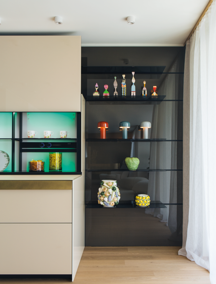 Floor-to-ceiling glass panels with open shelves in tinted glass surround the kitchen block with vertical sliding glass doors.